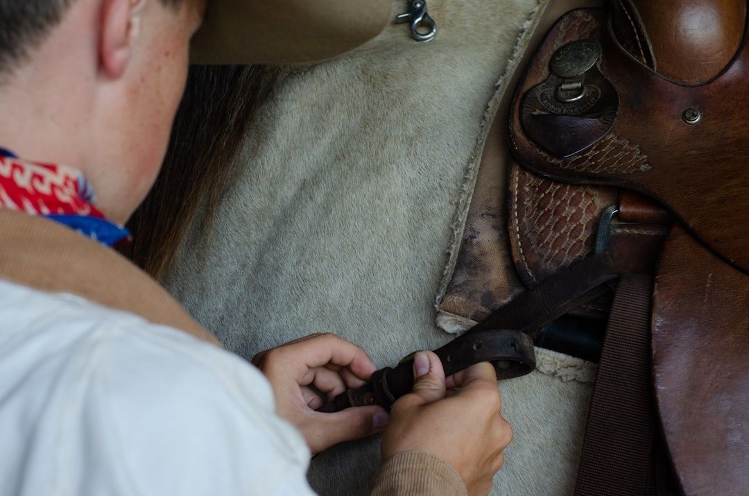 Person fastening a leather strap on a worn saddle